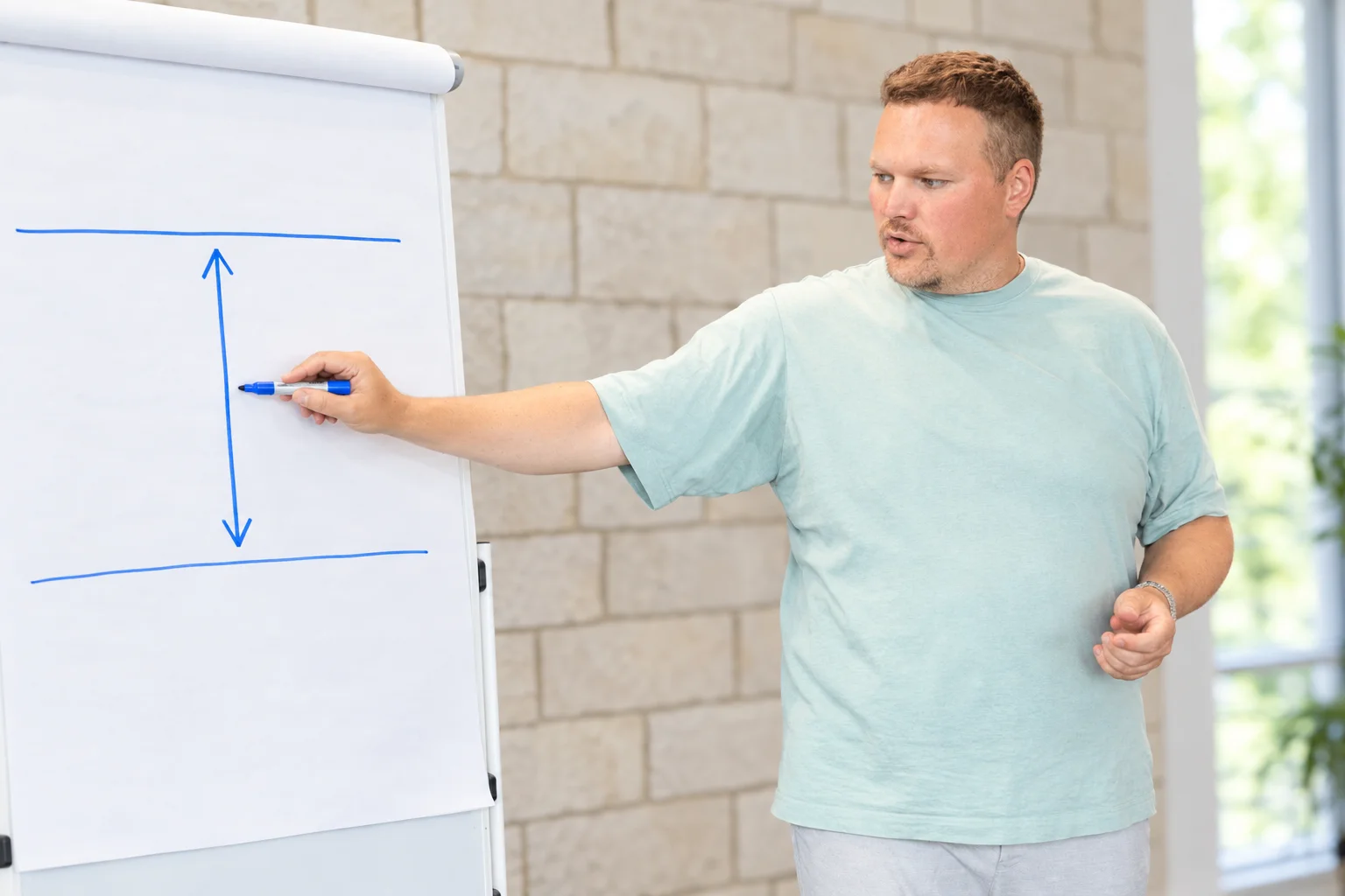 Sebastian Siedlecki am Flipchart. Er zeigt zwei Linien, Boden und Decke, mit einem Pfeil dazwischen.